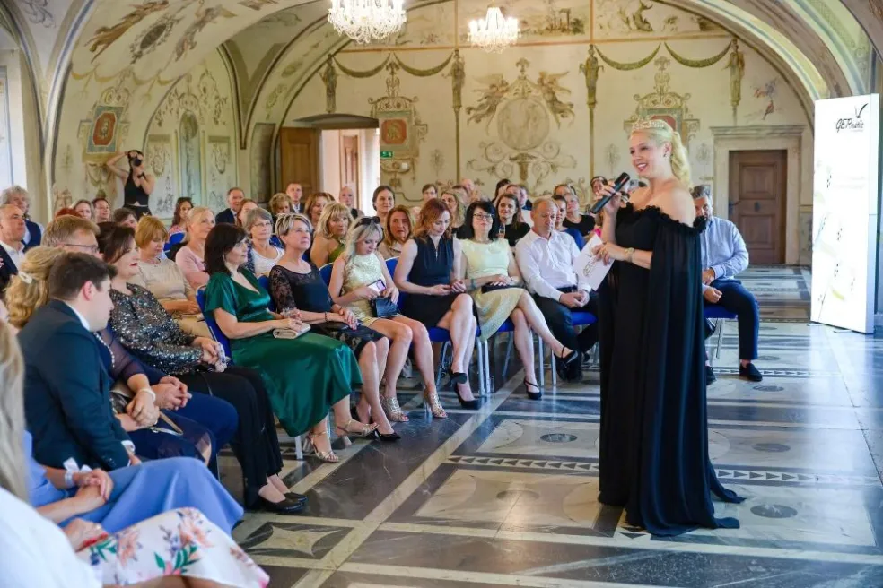 Moderátorka s mikrofonem zahajuje oslavu 30. výročí GERnétic v sále Martinického paláce v Praze.