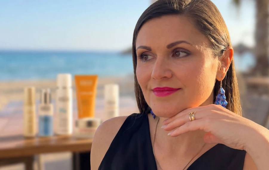 Henrieta Martinková, CEO značky ANNEMARIE BÖRLIND pre Slovensko a Česko, na pláži pri mori s opaľovacou kozmetikou na stole v pozadí