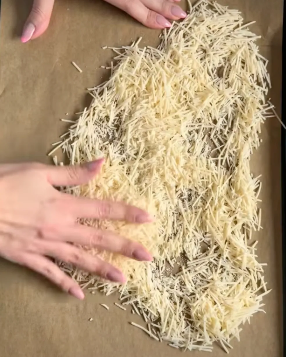 Nastrúhaný parmezán rozprestretý na papieri na pečenie pred vložením do rúry