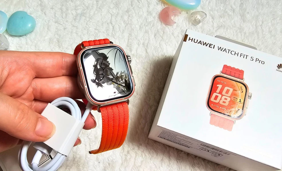 Huawei Watch Fit 5 Pro NFC v oranžovej farbe v otvorenom balení, produkt držiaci v ruke