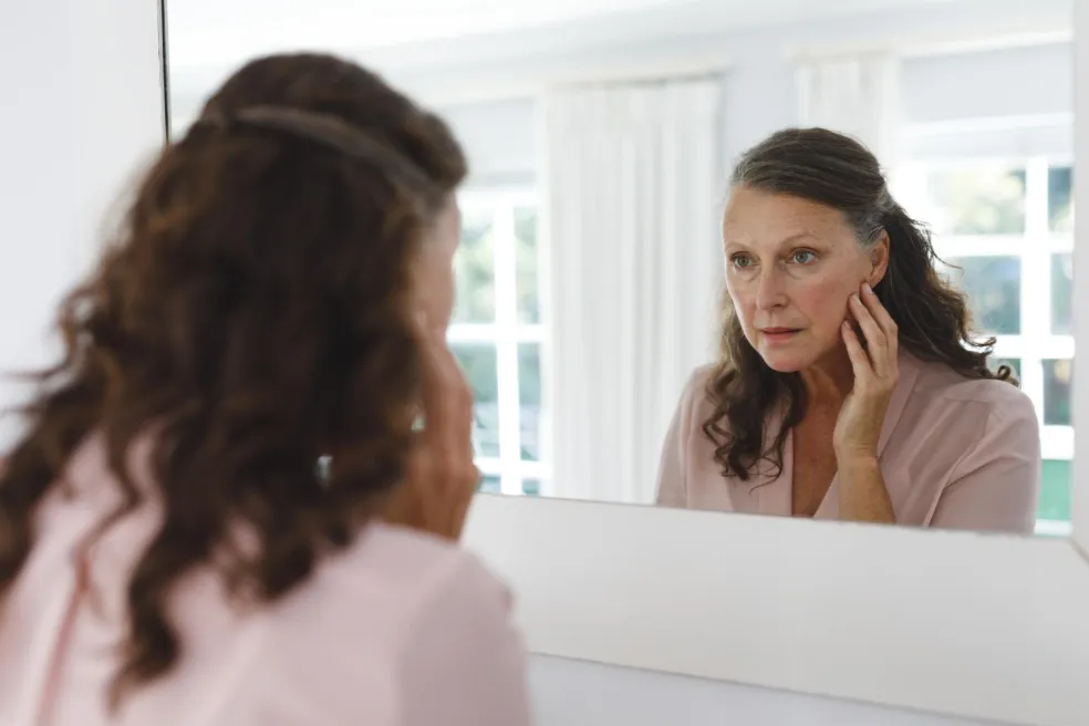 Žena si pred zrkadlom kontroluje stav pleti počas pravidelnej skincare rutiny