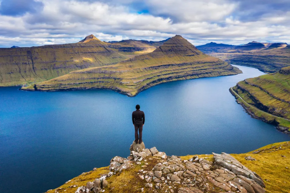 Turista obdivuje fjordy z hory pri obci Funningur na Faerských ostrovoch