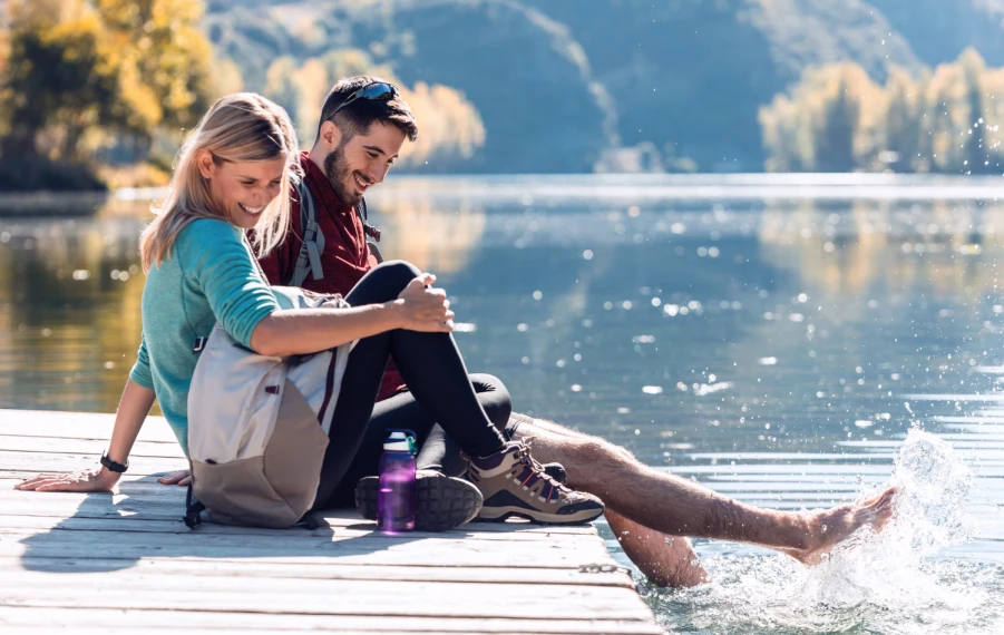 Šťastný pár oddychuje na slnečnom móle pri horskom jazere počas coolcation dovolenky