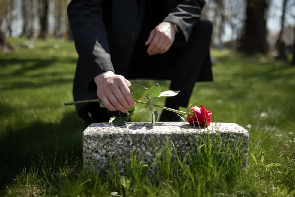 Muž v čiernom kladie červenú ružu na hrob na cintoríne