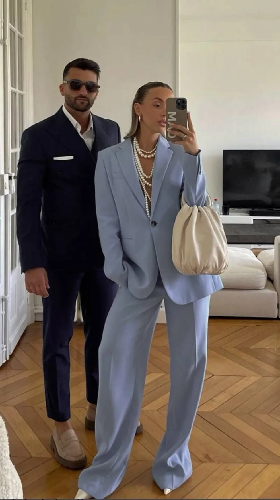 Pár v elegantnom business formal outfite – muž v tmavom obleku a žena v svetlom nohavicovom kostýme
