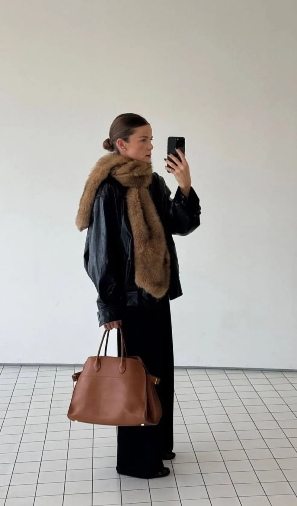 Žena v čiernom outfite s hnedým kožušinovým šálom okolo krku a hnedou kabelkou