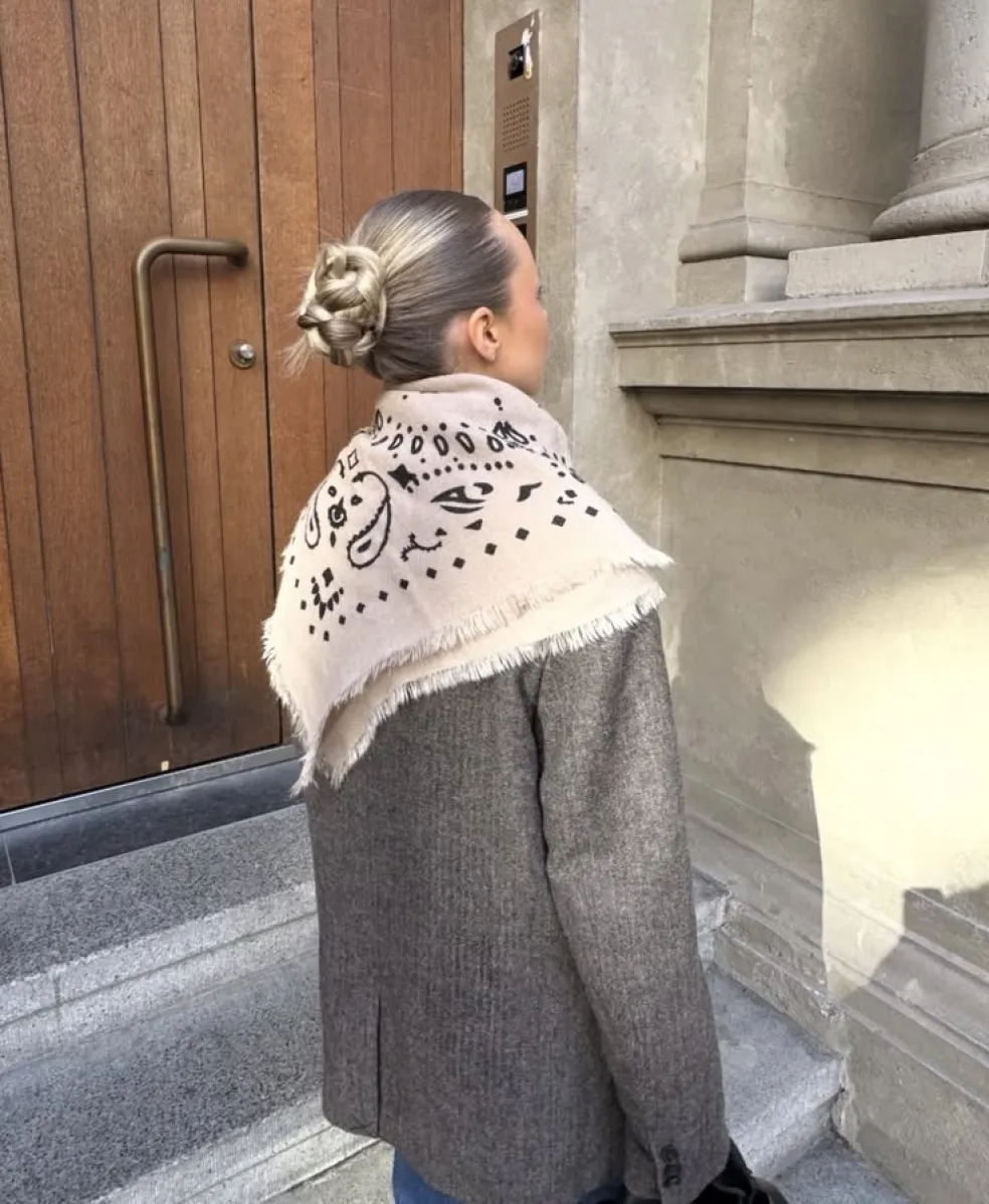 Žena so vzorovanou béžovou šatkou prehodenou cez ramená na sivom saku