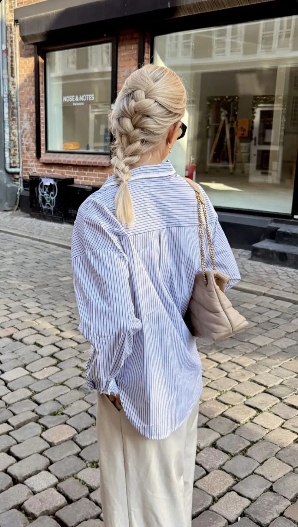 Polodlhé blond vlasy zapletené do voľného vrkoča zozadu počas prechádzky mestom