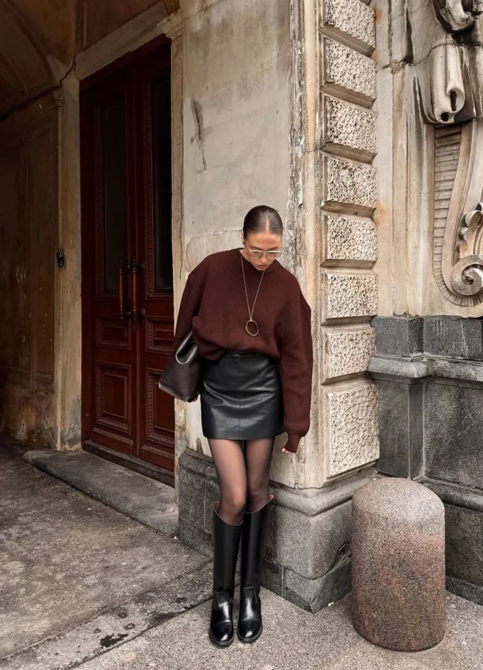 Čierna kožená mini sukňa s bordovým oversized svetrom, čiernymi pančuchami, vysokými čižmami a tmavou kabelkou v jesennom outfite