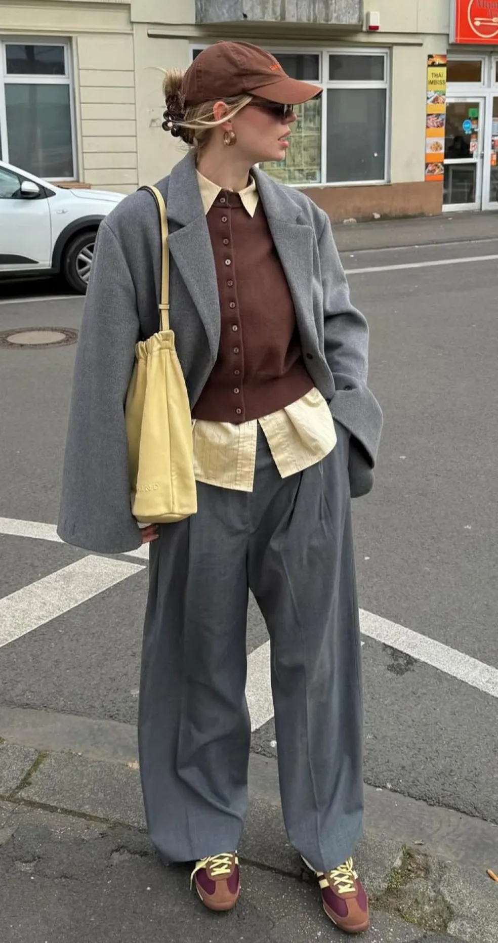 Žena v sivom oversize zimnom kabáte, širokých sivých nohaviciach a vrstvenom outfite na ulic