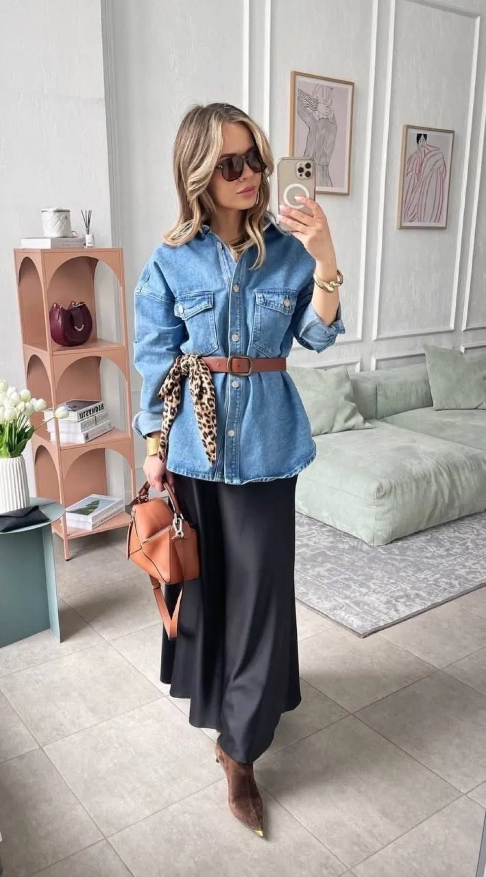 Jesenný outfit so svetlomodrou džínsovou košeľou zvýraznenou hnedým opaskom, čiernou saténovou midi sukňou a hnedými členkovými čižmami