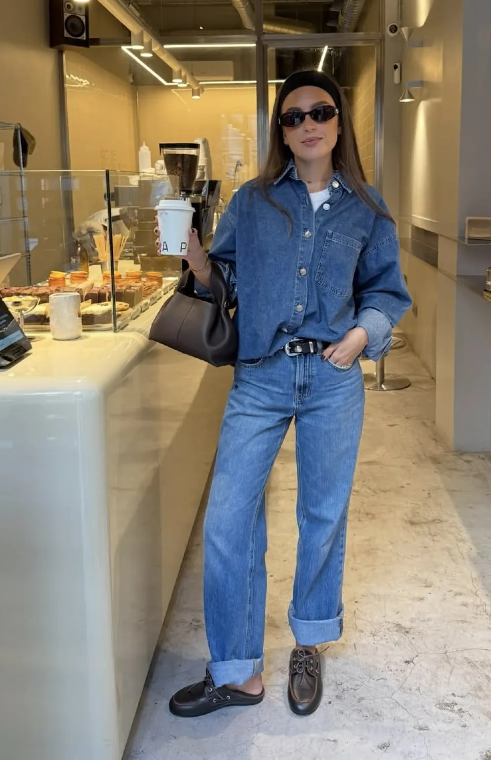 Denim on denim outfit s oversized modrou džínsovou košeľou, širokými džínsami s vyhrnutými lemami, čiernymi mokasínami a hnedou kabelkou