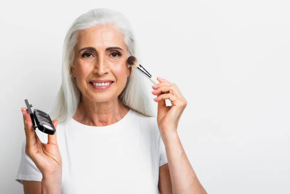 Zrelá žena pri prirodzenom líčení nanáša make-up štetcom na tvár