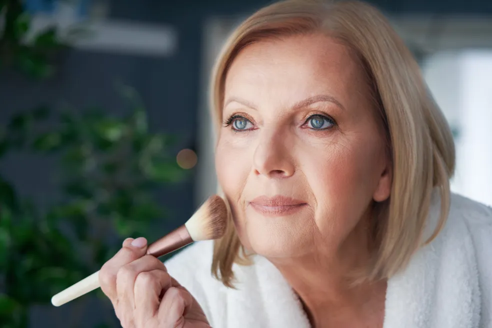 Zrelá žena nanáša púder štetcom na tvár pri prirodzenom líčení
