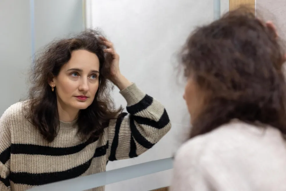 Žena si pred zrkadlom prezerá svoje tmavohnedé vlasy a kontroluje výsledok farbenia