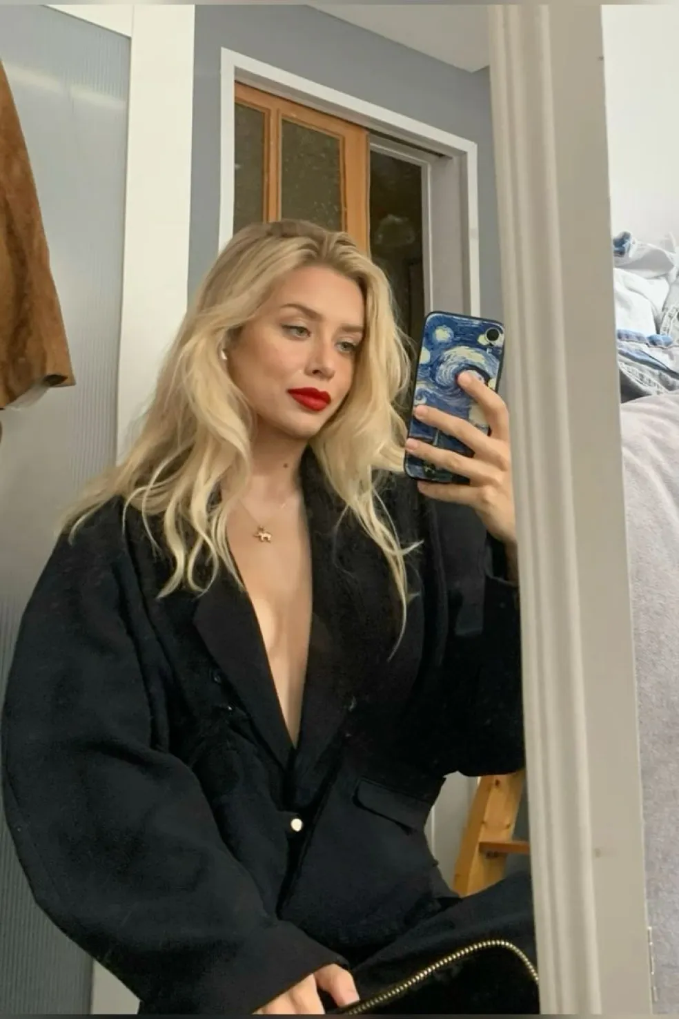 Blondínka s dlhými svetlými vlasmi, výrazným červeným rúžom a elegantným čiernym sakom pri fotografovaní v zrkadle