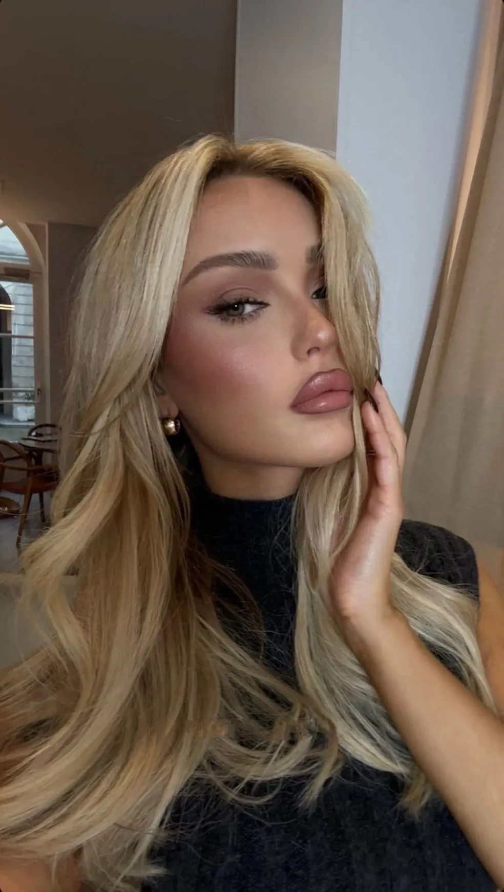Blondínka s dlhými svetlými vlasmi, výrazným líčením očí a lesklým ružovo-béžovým nude rúžom, ktorý zvýrazňuje kontúry pier