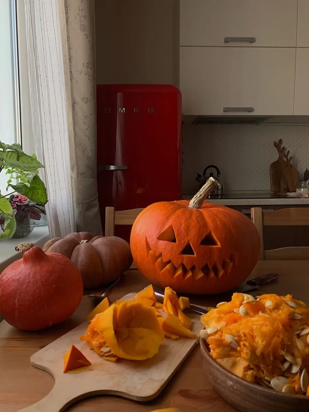 Vyrezávaná halloweenska tekvica so strašidelnou tvárou na kuchynskom stole, obklopená ďalšími tekvicami, dužinou a semienkami