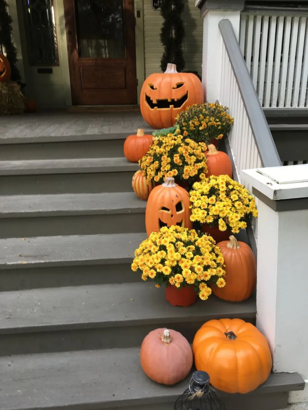 Halloweenska výzdoba schodov pred domom s vyrezávanými tekvicami, strašidelnými tvárami a žltými jesennými chryzantémami