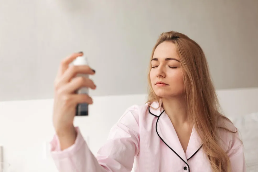 Žena so zatvorenými očami aplikuje fixačný sprej na tvár – použitie setting spray na zafixovanie make-upu a predĺženie výdrže líčenia