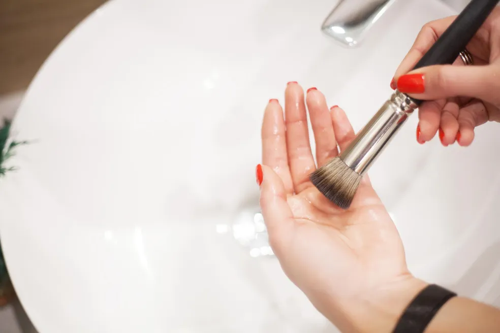 Čistenie kozmetického štetca v dlani nad umývadlom – správna hygiena štetcov na make-up a odstraňovanie zvyškov dekoratívnej kozmetiky