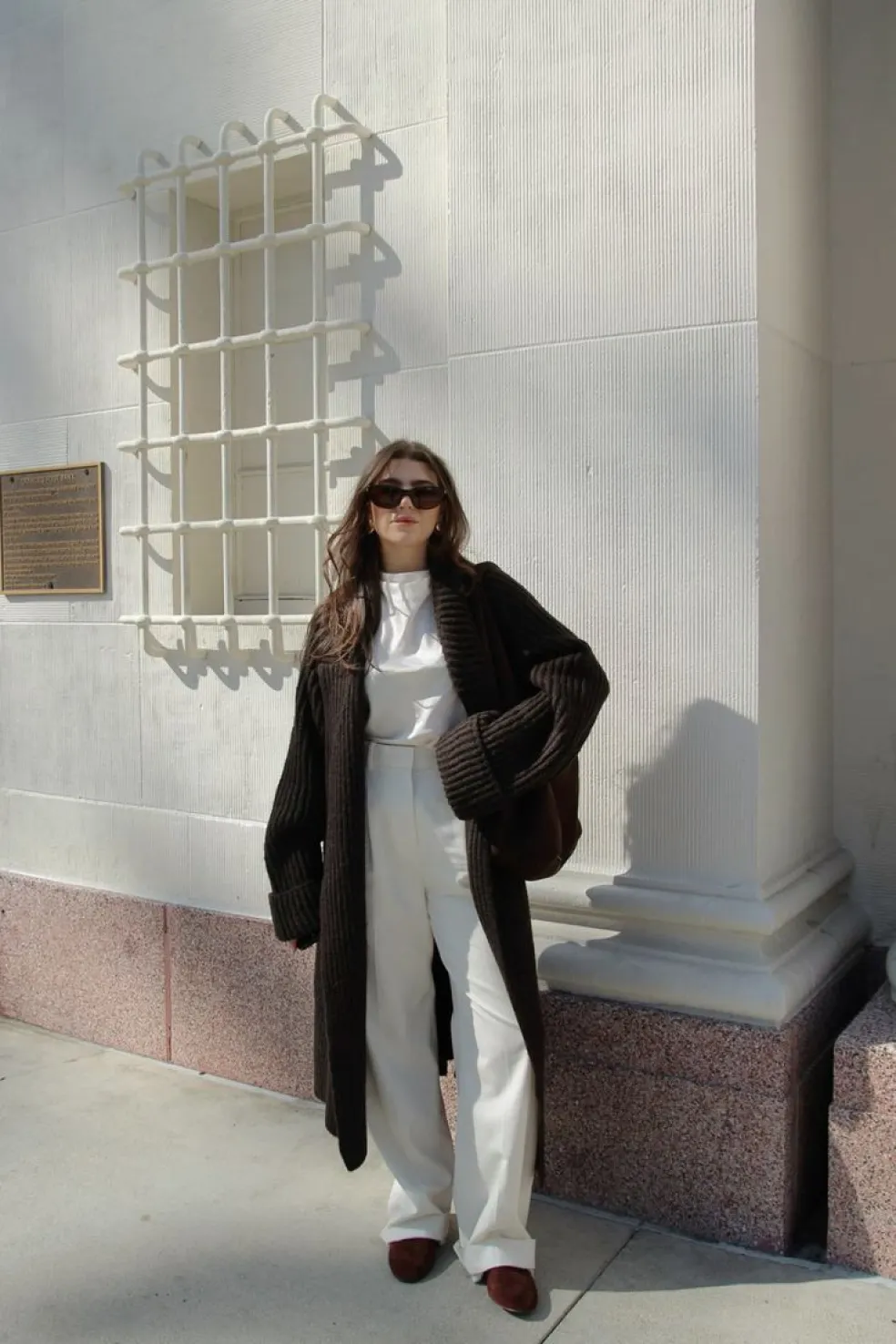 Žena v dlhom čokoládovohnedom maxi kardigáne, bielej blúzke a elegantných bielych nohaviciach – štýlový kancelársky outfit