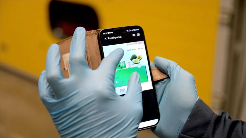 Ruky v rukaviciach ovládajú dozrievaciu komoru avokád cez aplikáciu v mobile