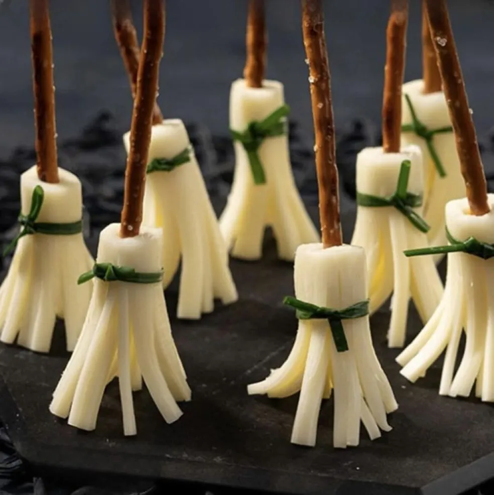 Slané jednohubky na Halloween v tvare čarodejníckych metličiek zo syra, slaných tyčiniek a pažítky na čiernom podnose