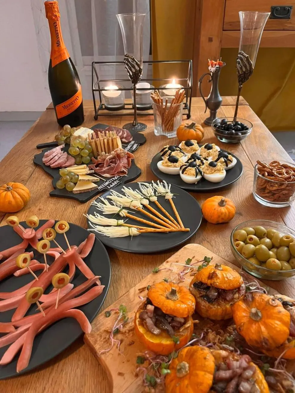 Halloweenské slané občerstvenie naaranžované na párty stole – syrové metličky, pavúčiky z olív, plnené tekvice, mäsové pochúťky a tematické dekorácie